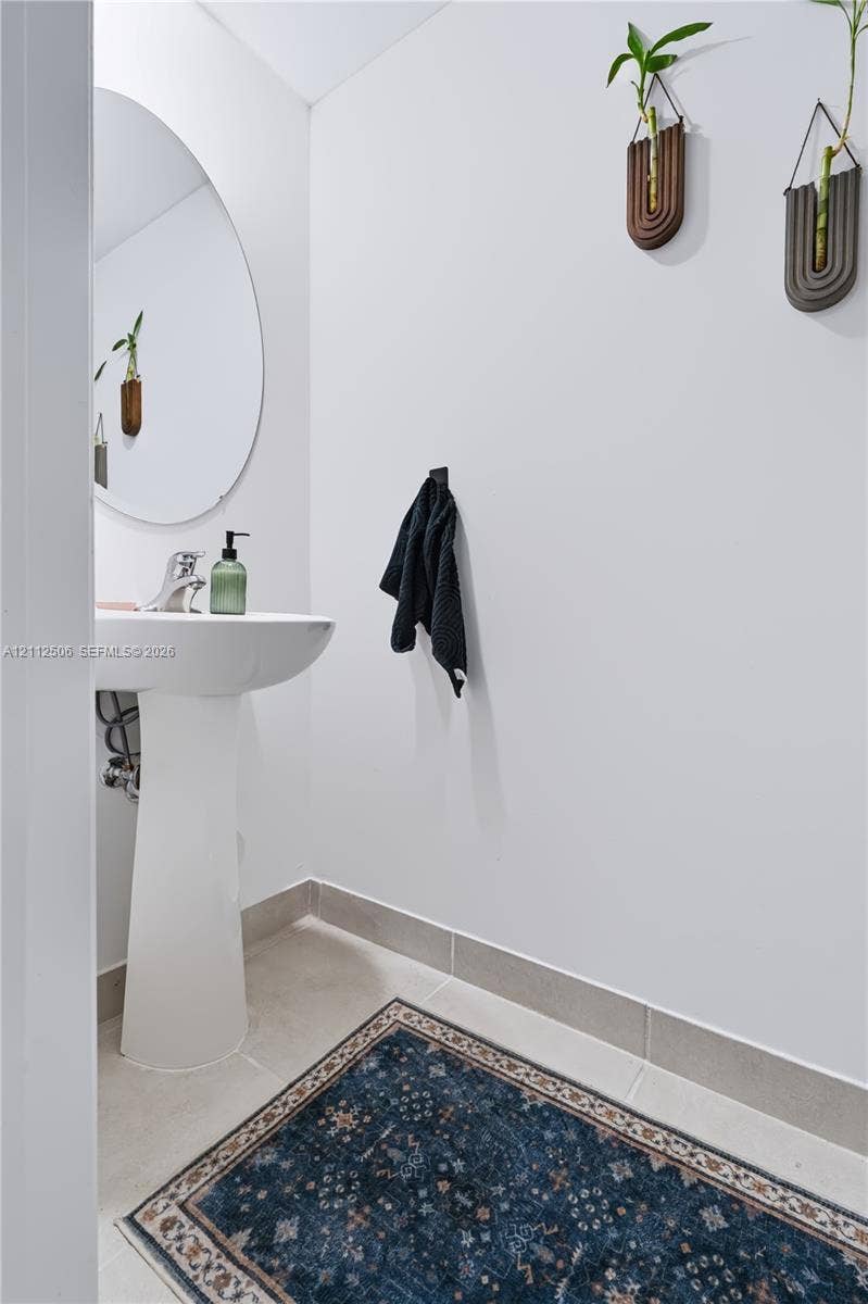 538 SW 19th Terrace, Fort Lauderdale, Fort Lauderdale, FL 33312 Pedestal sink with a single-handle chrome faucet, frameless circular wall mirror, and neutral tile flooring with coordinated tile baseboards