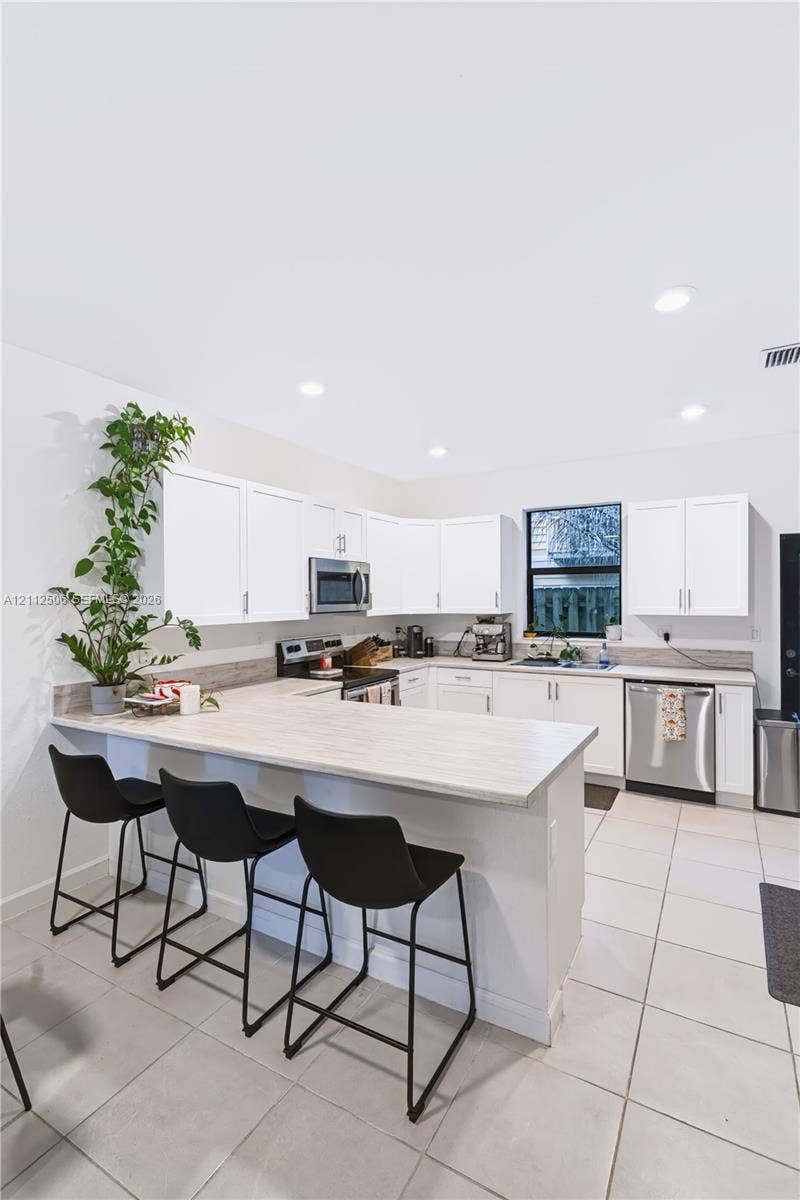 538 SW 19th Terrace, Fort Lauderdale, Fort Lauderdale, FL 33312 Kitchen featuring white shaker-style cabinetry, a wraparound breakfast bar, stainless steel appliances, neutral stone-finish countertops, and ceramic tile flooring