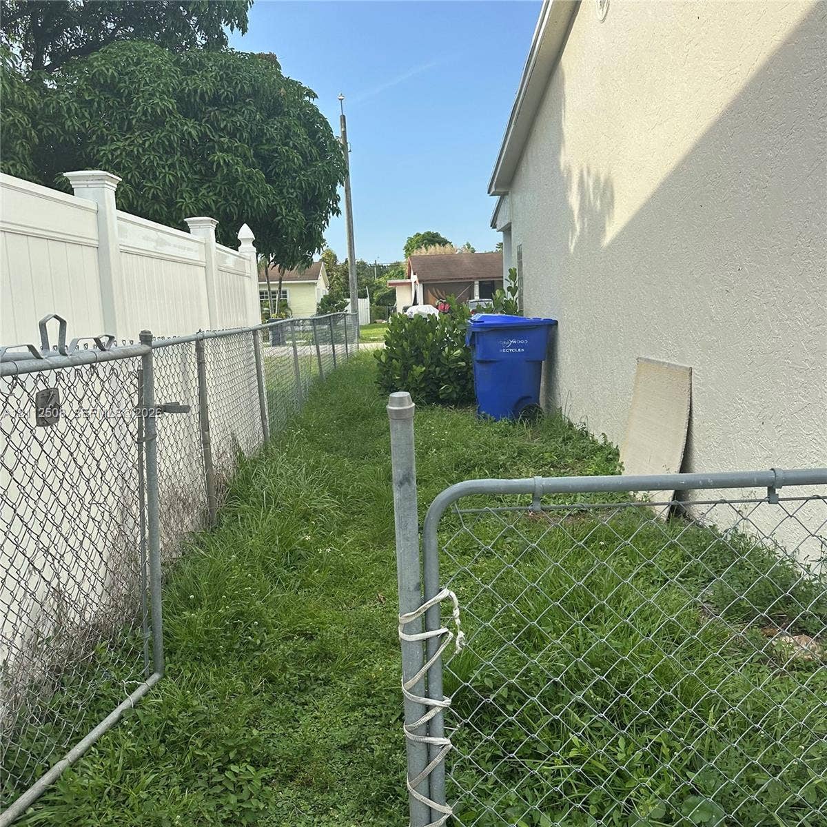 6432 Flagler Street, #1, Hollywood, Hollywood, FL 33023 Exterior side yard area featuring a stucco wall finish, white vinyl privacy fencing, and chain-link metal fencing