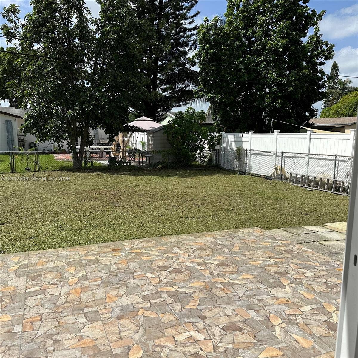 6432 Flagler Street, #1, Hollywood, Hollywood, FL 33023 Backyard featuring a stone-patterned patio, grass lawn, mature trees, and white vinyl privacy fencing