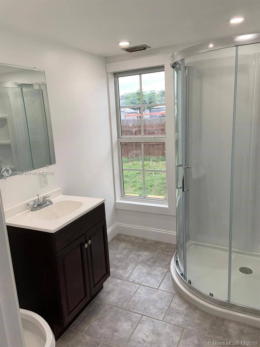 215 4th Street, #1, Jupiter, Jupiter, FL 33458 Bathroom featuring a dark wood-finish vanity, light-toned countertop with an integrated sink, curved glass-enclosed shower, and tile flooring