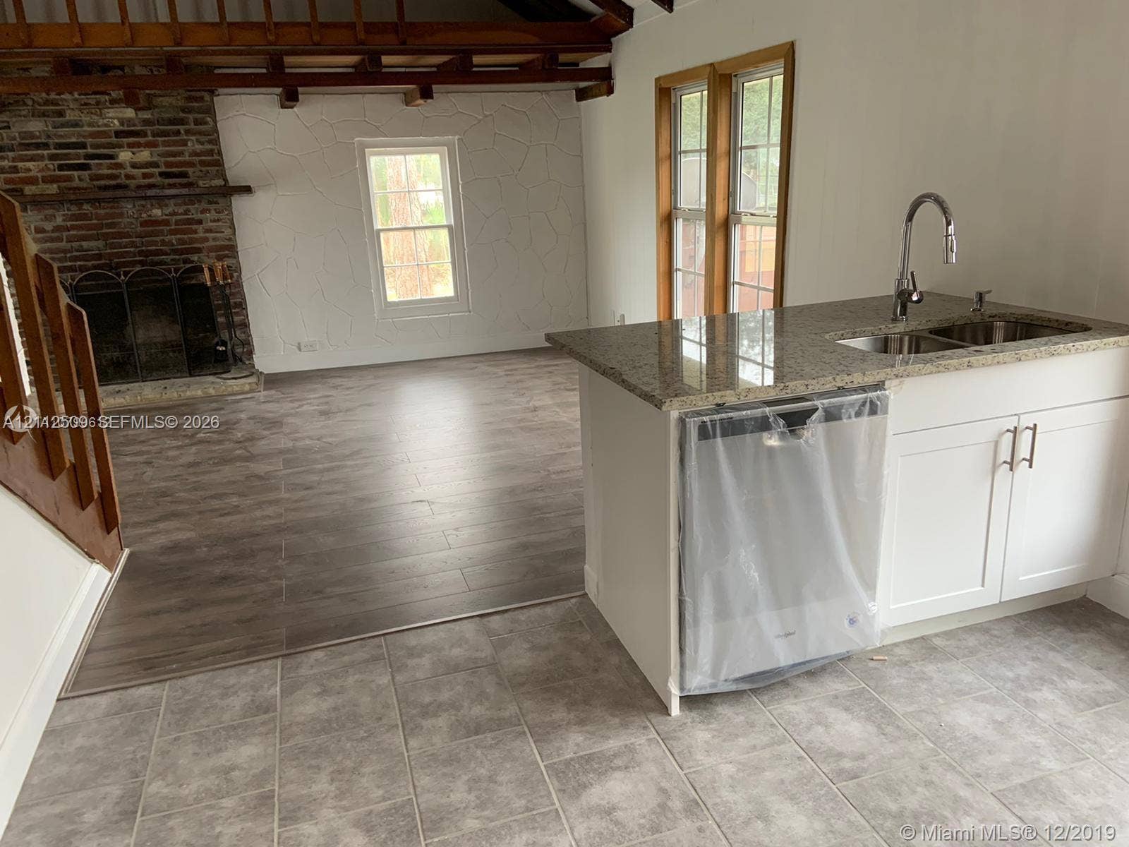 215 4th Street, #1, Jupiter, Jupiter, FL 33458 Kitchen island featuring stone countertops, integrated stainless steel sink, and white cabinetry, paired with wood-finish flooring, a full-height brick fireplace, and exposed structural ceiling beams