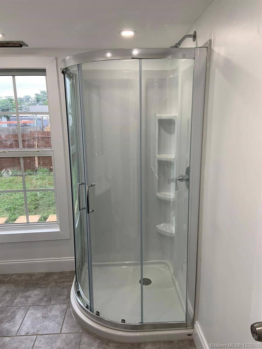 215 4th Street, #1, Jupiter, Jupiter, FL 33458 Corner shower stall featuring a curved sliding glass door, white surround with built-in shelving, chrome-finish hardware, and tile flooring