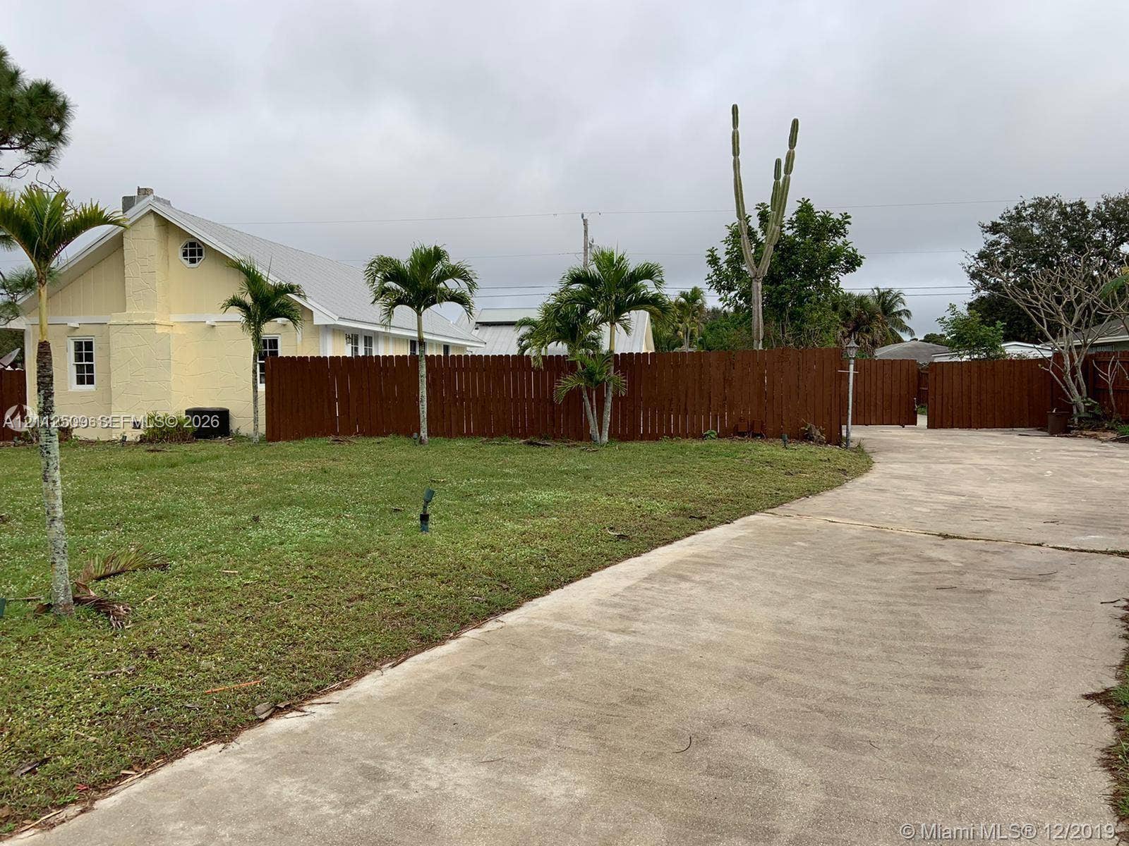 215 4th Street, #1, Jupiter, Jupiter, FL 33458 Exterior featuring pale yellow siding, a concrete driveway, a wood-slat privacy fence, and native palm landscaping