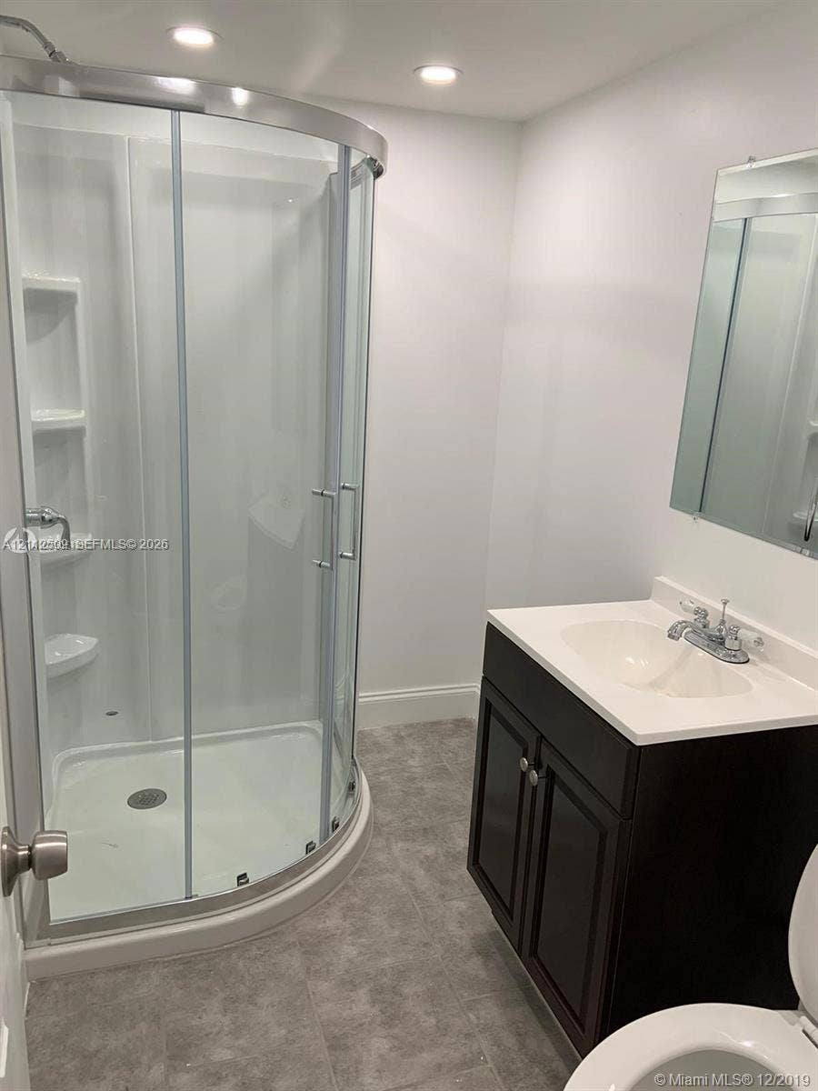 215 4th Street, #1, Jupiter, Jupiter, FL 33458 Curved glass shower enclosure with integrated shelving, dark wood-finish cabinetry, solid-surface vanity countertop, recessed lighting, and large wall-mounted mirror