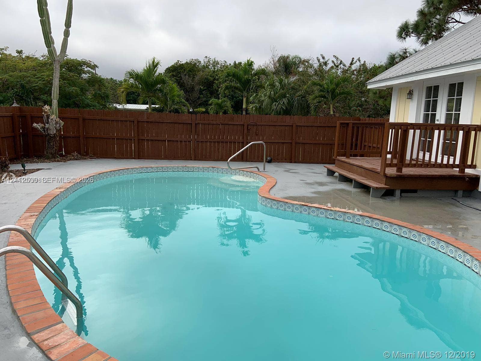215 4th Street, #1, Jupiter, Jupiter, FL 33458 Curved in-ground pool with decorative tile border and brick coping, elevated wood deck, and perimeter wood privacy fencing