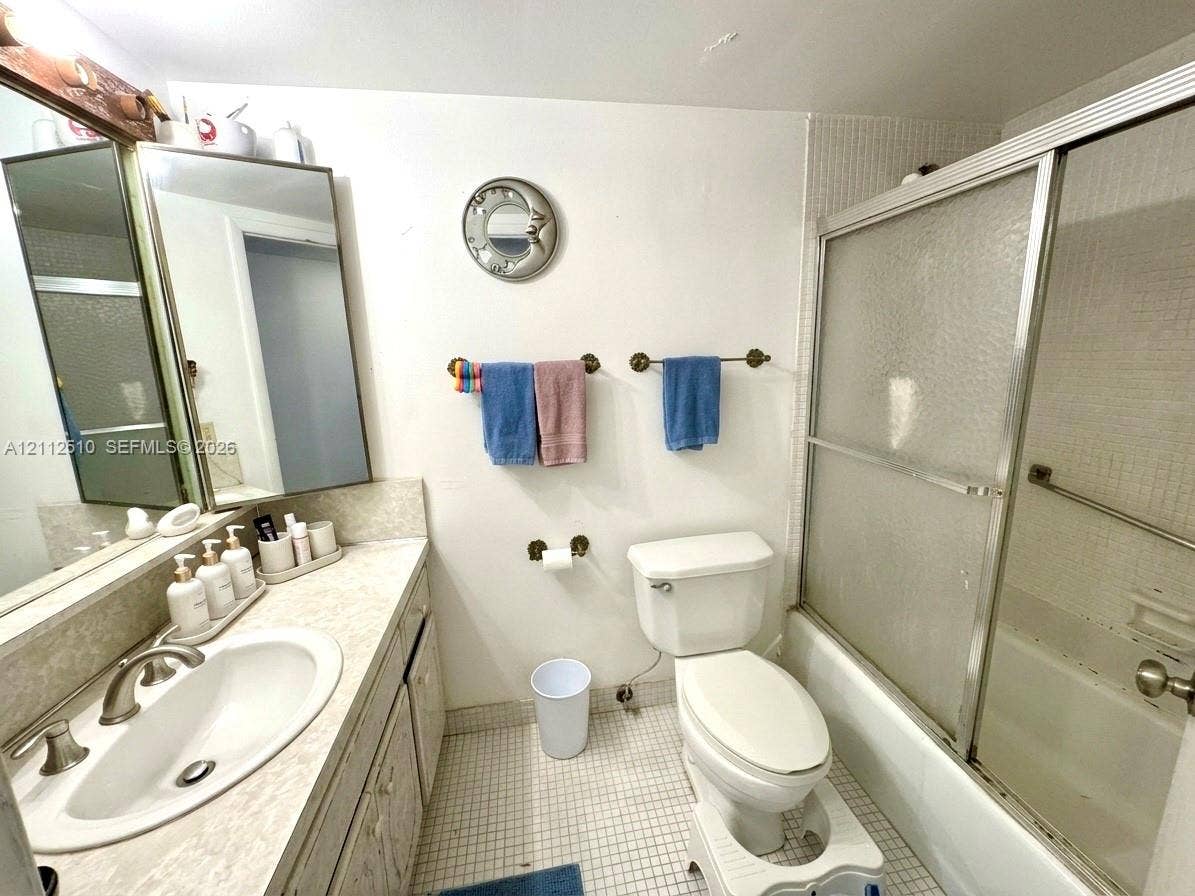 9250 W Bay Harbor Drive, #4A, Bay Harbor Islands, FL 33154 Bathroom featuring a vanity with an integrated oval sink, countertop, tri-panel mirrored cabinet, mosaic tile flooring, and a tub-shower combination with sliding glass doors