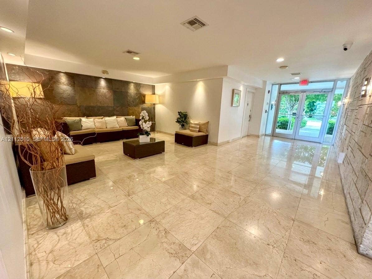 9250 W Bay Harbor Drive, #4A, Bay Harbor Islands, FL 33154 Lobby featuring polished stone flooring, large-format dark stone accent wall, light-toned stone textured wall, recessed lighting, and glass-paneled double entrance doors
