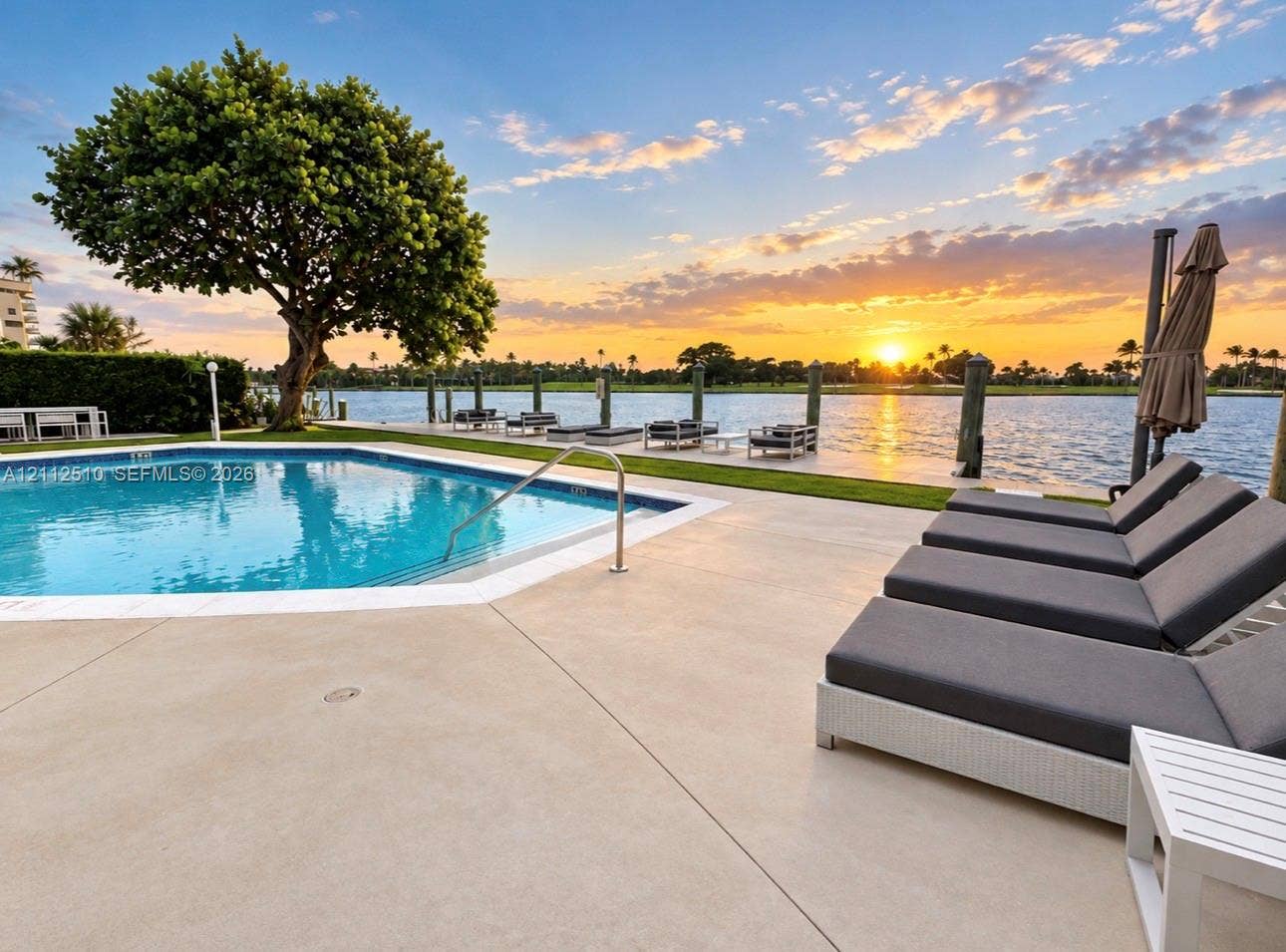 9250 W Bay Harbor Drive, #4A, Bay Harbor Islands, FL 33154 In-ground swimming pool with a concrete surround, mature tree, private dock, and waterway backdrop
