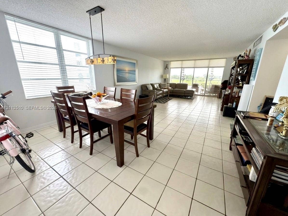 9250 W Bay Harbor Drive, #4A, Bay Harbor Islands, FL 33154 Open-concept living and dining area featuring expansive floor-to-ceiling windows, ceramic tile flooring, and a contemporary linear chandelier