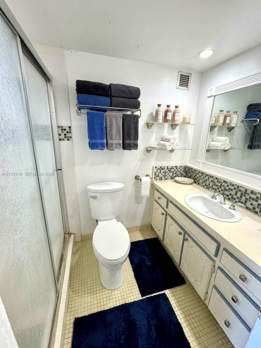 9250 W Bay Harbor Drive, #4A, Bay Harbor Islands, FL 33154 Bathroom featuring a shower stall with semi-transparent enclosure, vanity with integrated sink, glass shelving, framed mirror, and mosaic tile backsplash