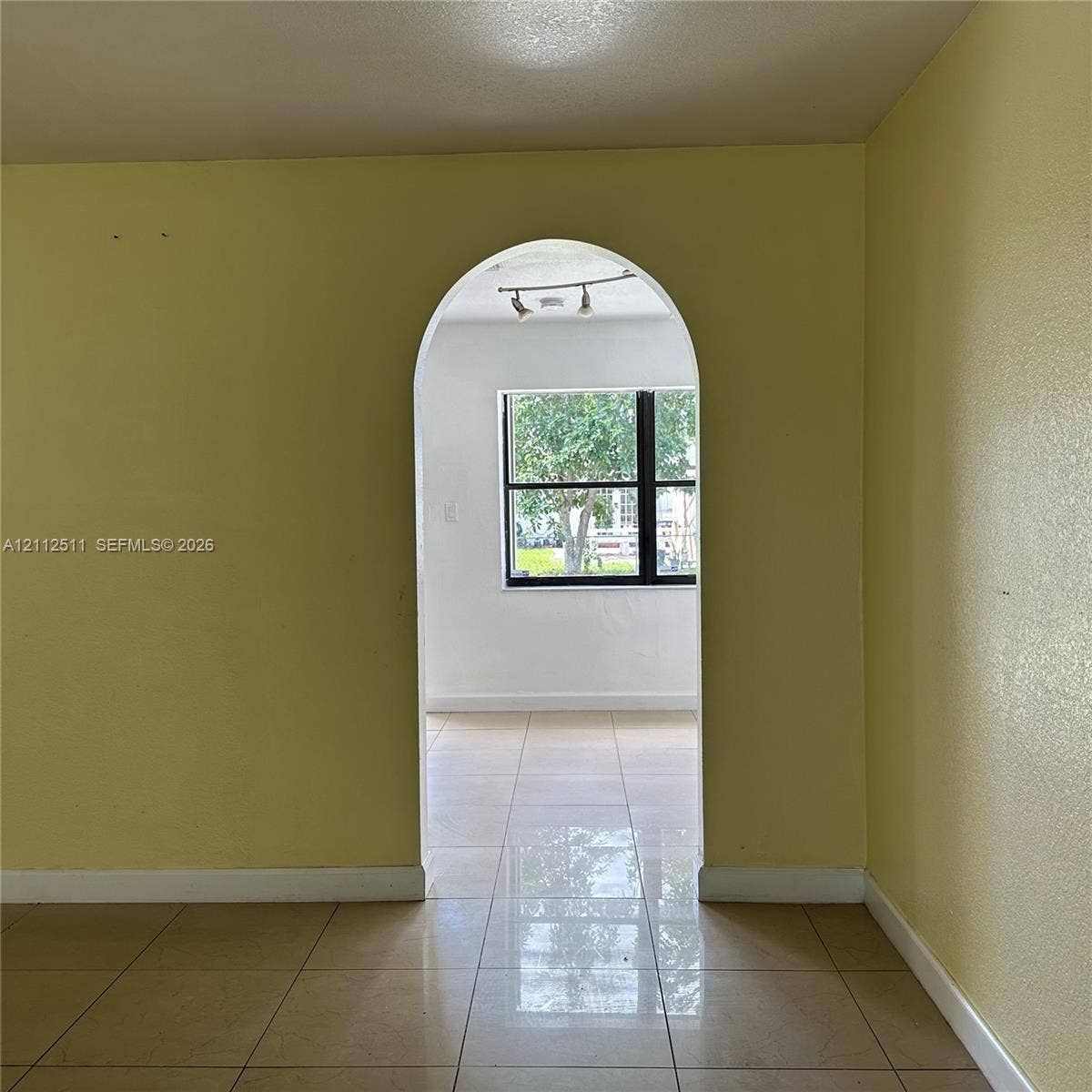 Architectural arched doorway with large-format tile flooring, multi-light track lighting, and a prominent window
