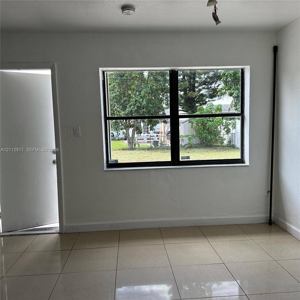 Interior space featuring light-colored tile flooring, smooth wall finishes, and a large horizontal window with black framing