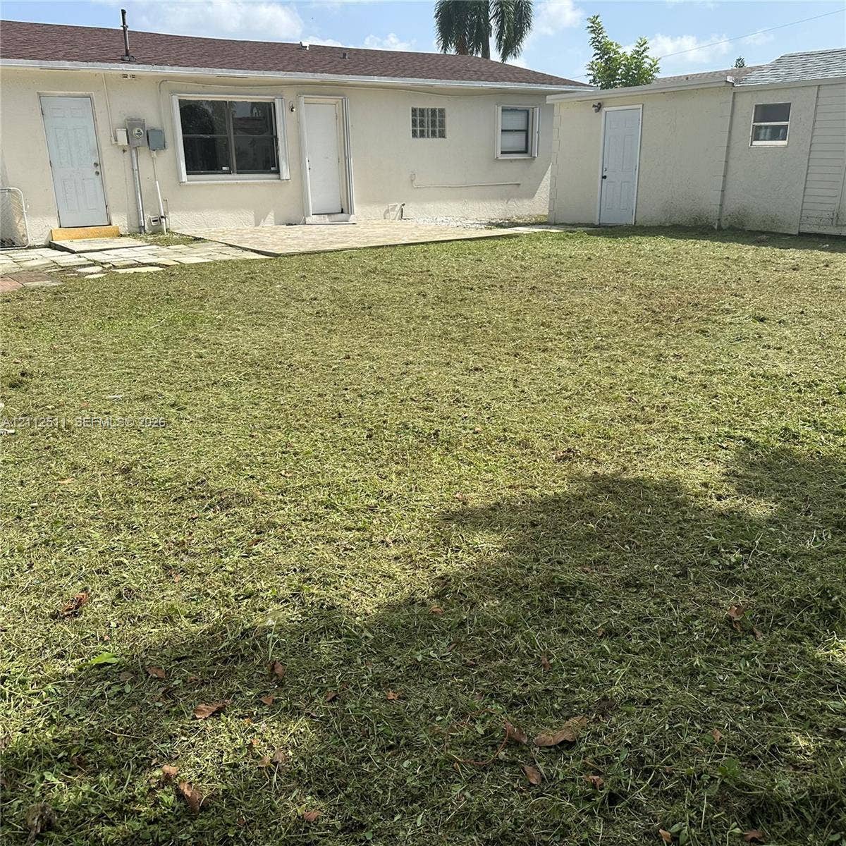 Expansive backyard featuring a concrete patio, detached storage structure, and stucco exterior walls
