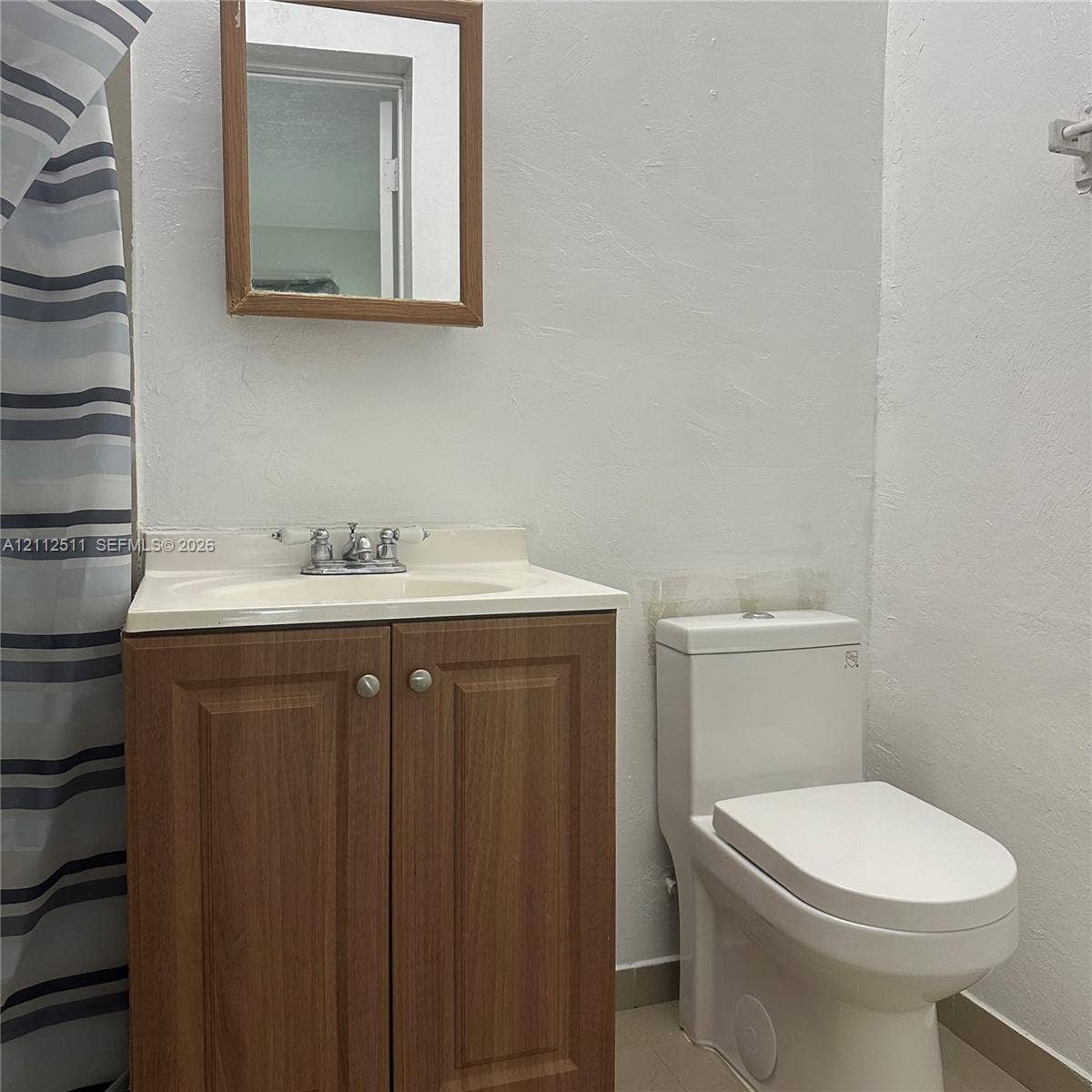 Bathroom featuring a wood-finish vanity cabinet, integrated sink with a chrome dual-handle faucet, rectangular wood-framed wall mirror, and a white one-piece toilet