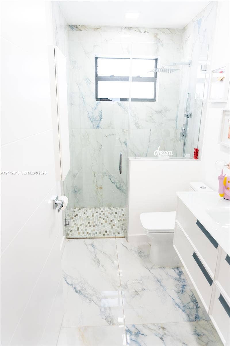 Hallandale Beach, FL 33009 Bathroom featuring large-format veined tile flooring, a glass-enclosed shower with mosaic tile floor, a wall-mounted floating vanity, and a minimalist toilet