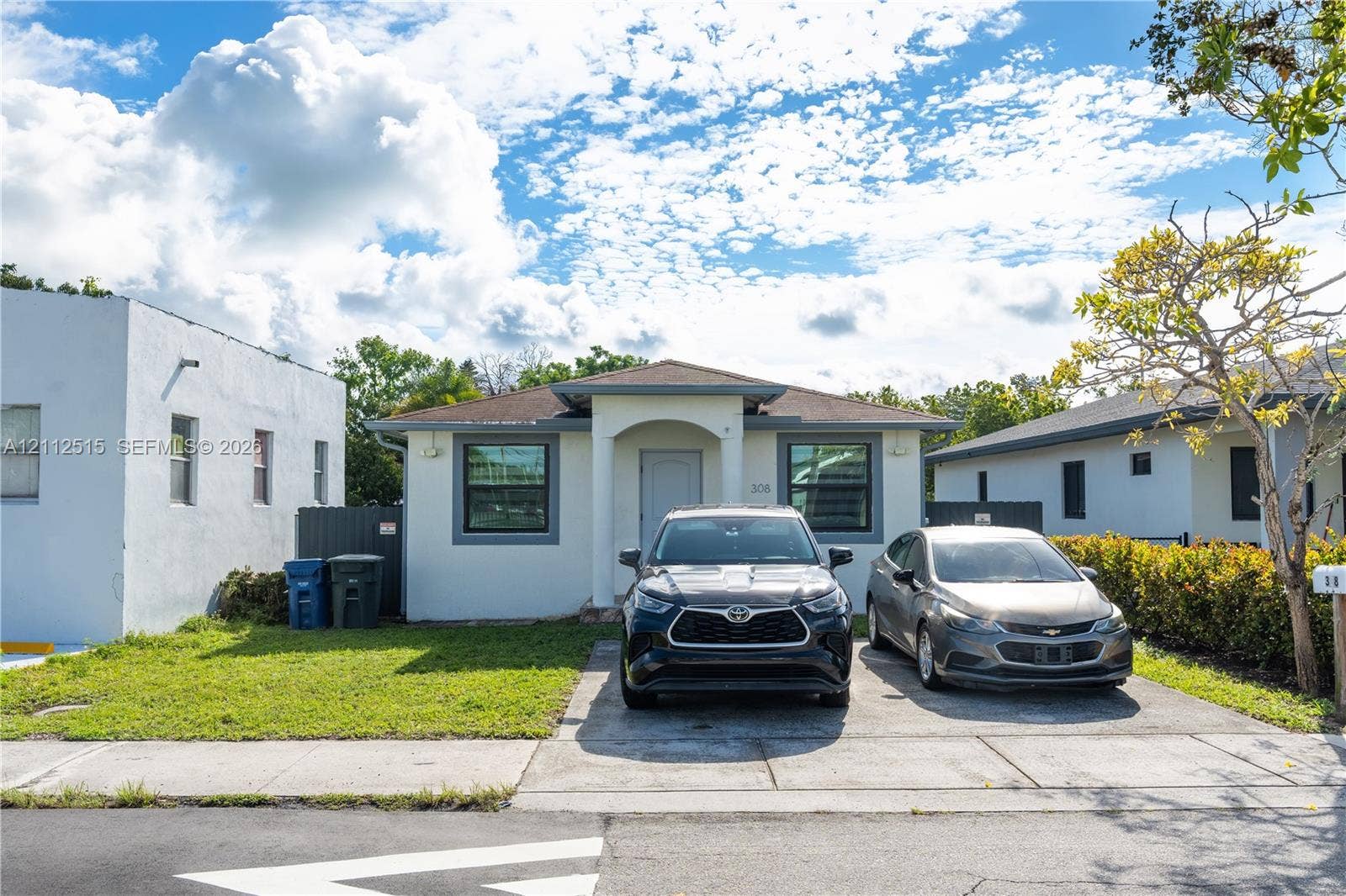 Hallandale Beach, FL 33009 Single-story exterior featuring a stucco facade, covered entryway with arched detailing, concrete driveway, and a hipped roof
