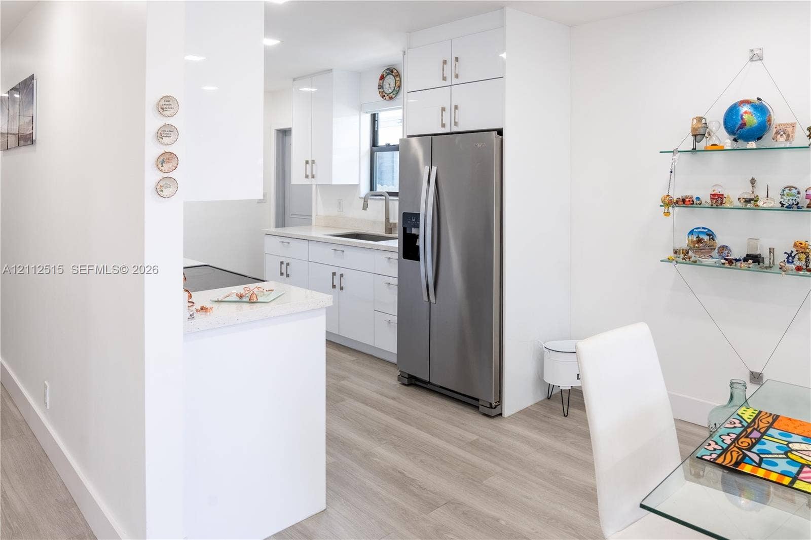 Hallandale Beach, FL 33009 Kitchen featuring high-gloss white cabinetry, stainless steel side-by-side refrigerator, light-toned stone-finish countertops, and wood-finish flooring