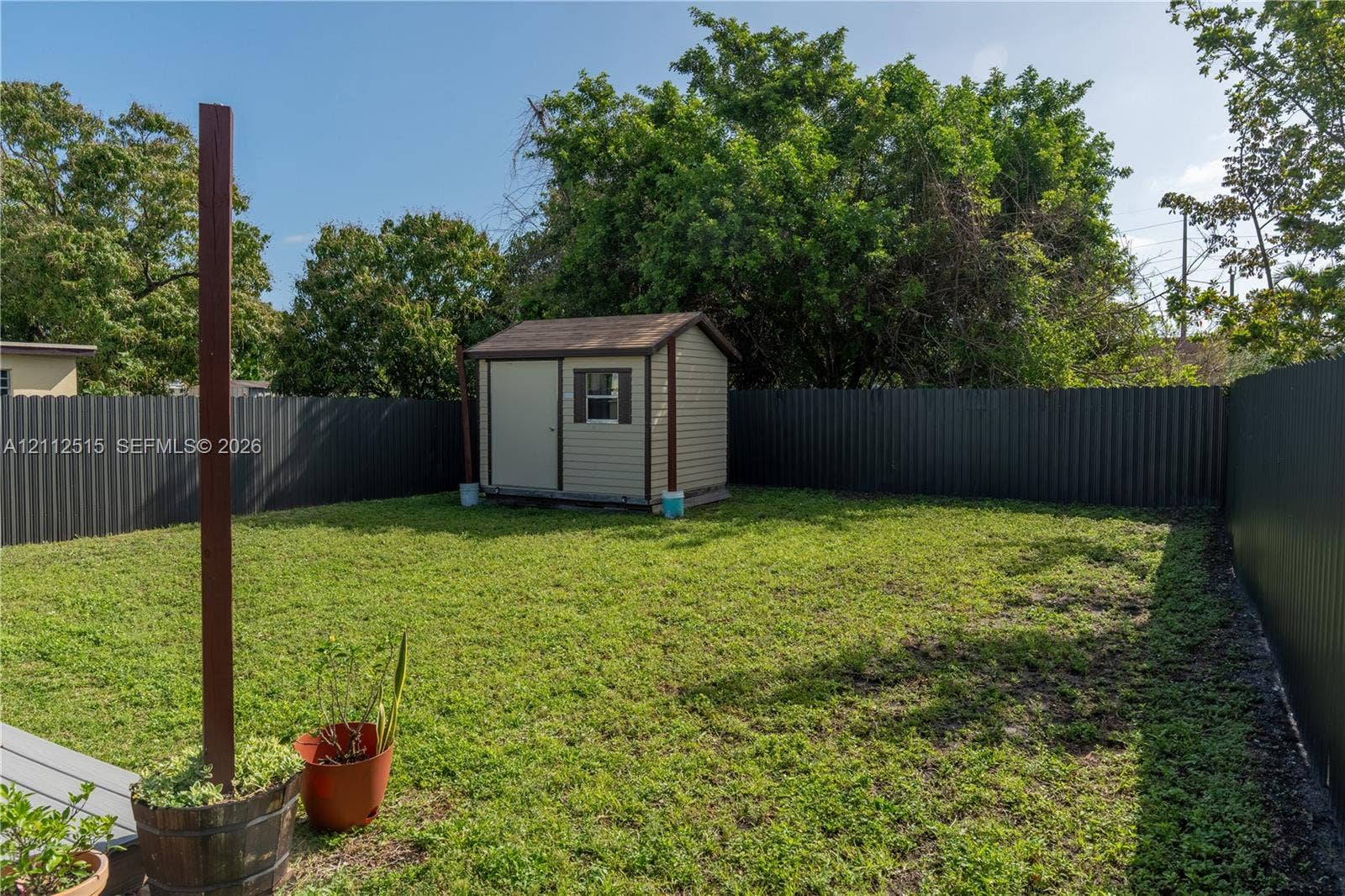 Hallandale Beach, FL 33009 Backyard featuring a detached storage shed, privacy fencing, and mature trees