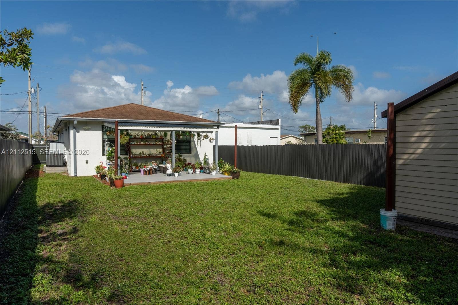 Hallandale Beach, FL 33009 Rear exterior featuring a concrete patio, a covered pergola, and a private metal perimeter fence surrounding the lawn