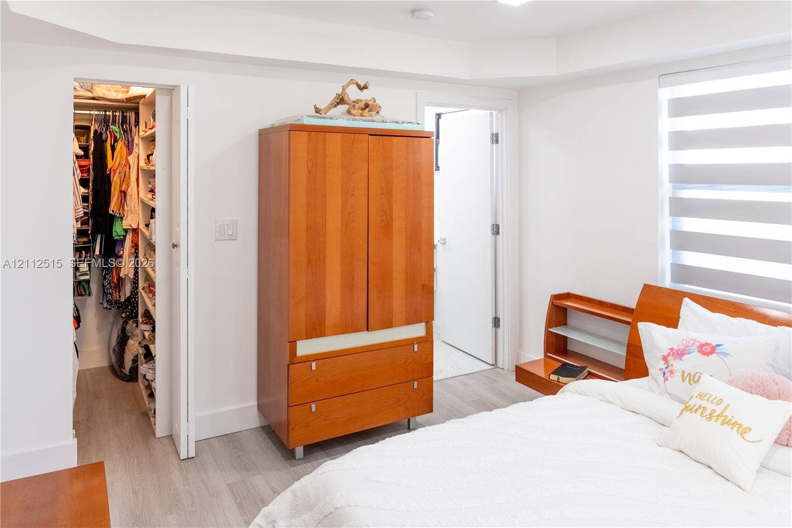 Hallandale Beach, FL 33009 Bedroom featuring wood-finish flooring, tray ceiling, and dual-layered window shades