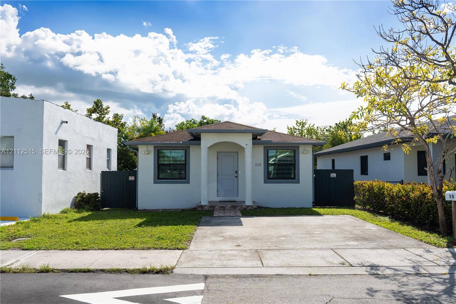 Hallandale Beach, FL 33009 Single-story exterior featuring a stucco facade, covered front entryway with architectural pillars, concrete driveway, and gated side access