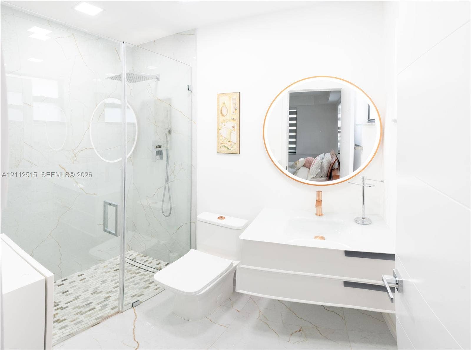 Hallandale Beach, FL 33009 Floating vanity with a smooth white countertop, large-format stone-patterned wall tiles, glass-enclosed walk-in shower, pebble-mosaic shower flooring, and a circular wall-mounted mirror
