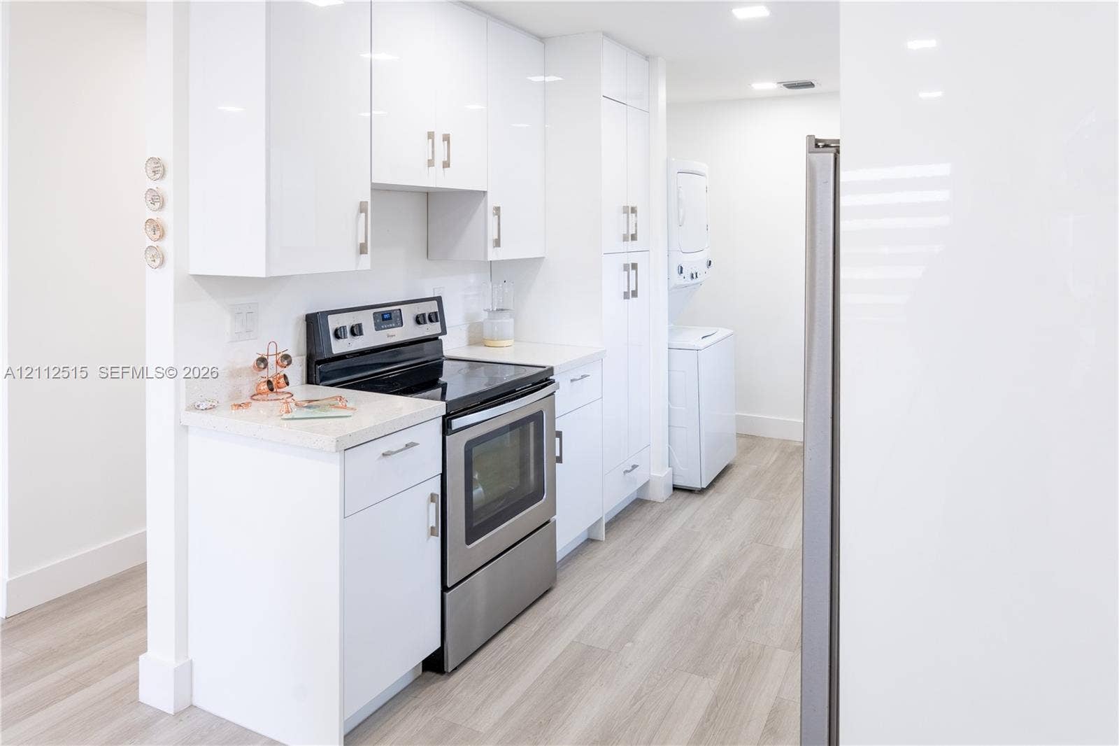 Hallandale Beach, FL 33009 Kitchen featuring white slab-front cabinetry, stainless steel range, light-toned stone-finish countertops, wood-finish flooring, and recessed ceiling lighting