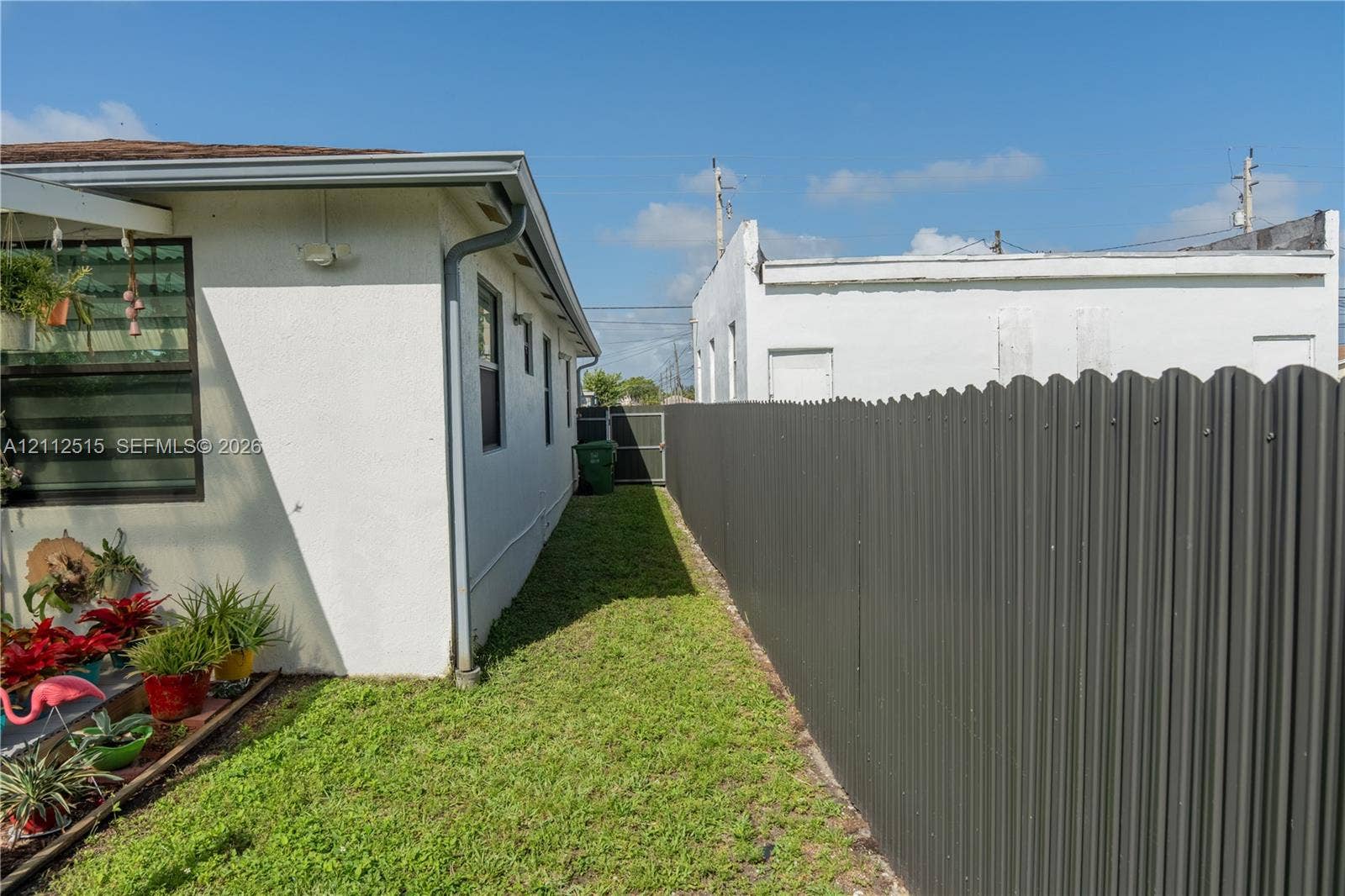 Hallandale Beach, FL 33009 Exterior side yard featuring a stucco-finished wall, corrugated metal privacy fencing, and a sodded lawn area
