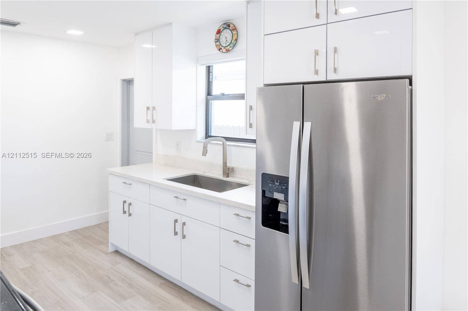 Hallandale Beach, FL 33009 Kitchen featuring high-gloss white cabinetry, solid-surface countertops, stainless steel side-by-side refrigerator, under-mount sink with gooseneck faucet, and wood-finish flooring