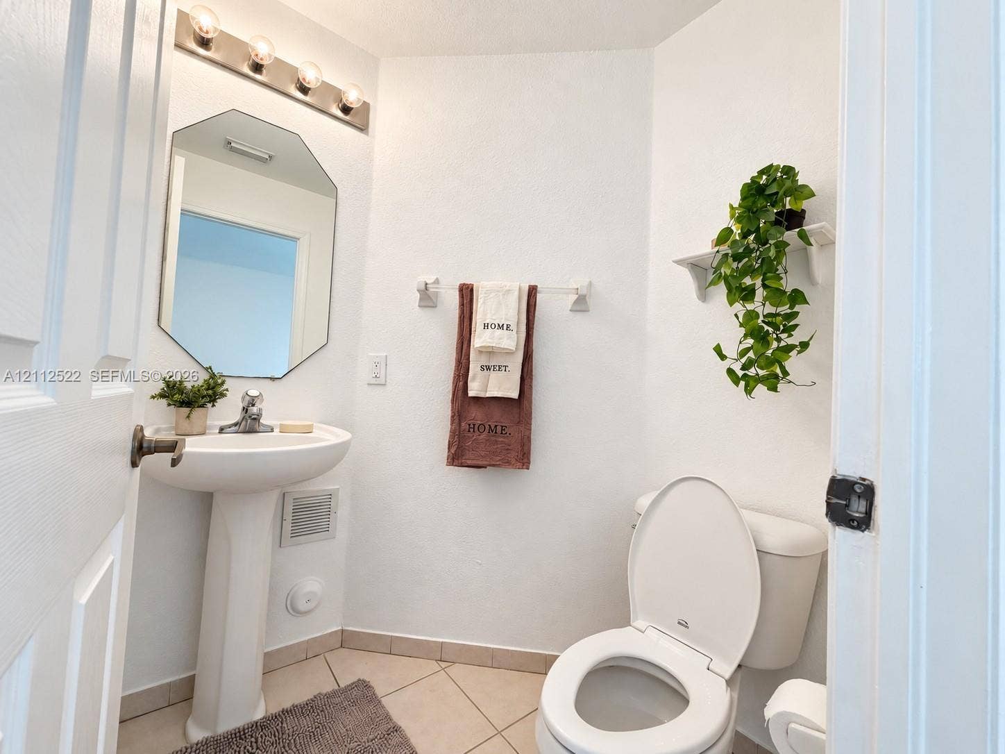 7822 NW 116th Avenue, Doral, FL 33178 Pedestal sink with chrome faucet, octagonal wall mirror, four-bulb vanity lighting fixture, tile flooring, and wall-mounted shelving