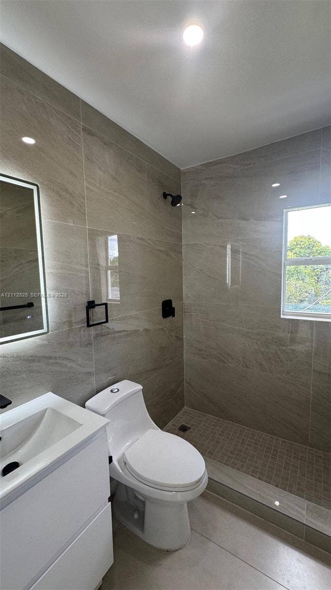 351 E 14th Street, #353, Hialeah, Hialeah, FL 33010 Large-format stone-style wall tiling, walk-in shower with mosaic tile flooring, contemporary white vanity, backlit mirror, and matte black hardware