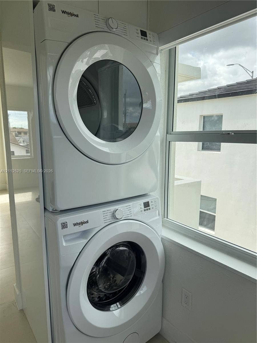 351 E 14th Street, #353, Hialeah, Hialeah, FL 33010 Stacked Whirlpool washer and dryer unit featuring digital controls and front-loading glass doors, positioned near a large window with white-frame casing