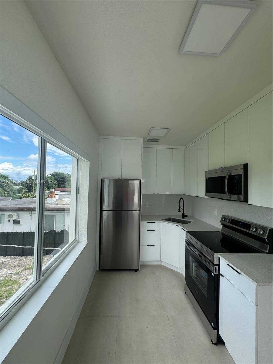 351 E 14th Street, #353, Hialeah, Hialeah, FL 33010 Kitchen featuring white high-gloss cabinetry, stainless steel appliances, solid-surface countertops, a matte black faucet, and expansive windows