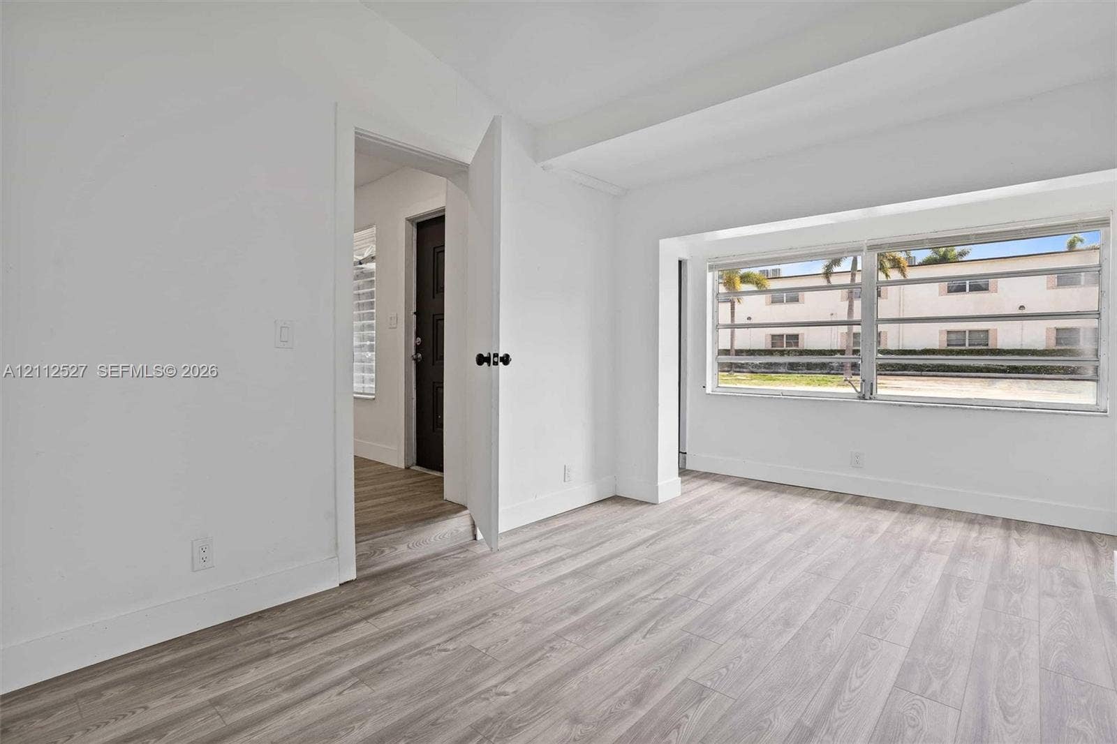 2517 Polk Street, Hollywood, Hollywood, FL 33020 Interior space featuring wood-finish flooring, large window with horizontal blinds, and a solid-core door with matte black hardware