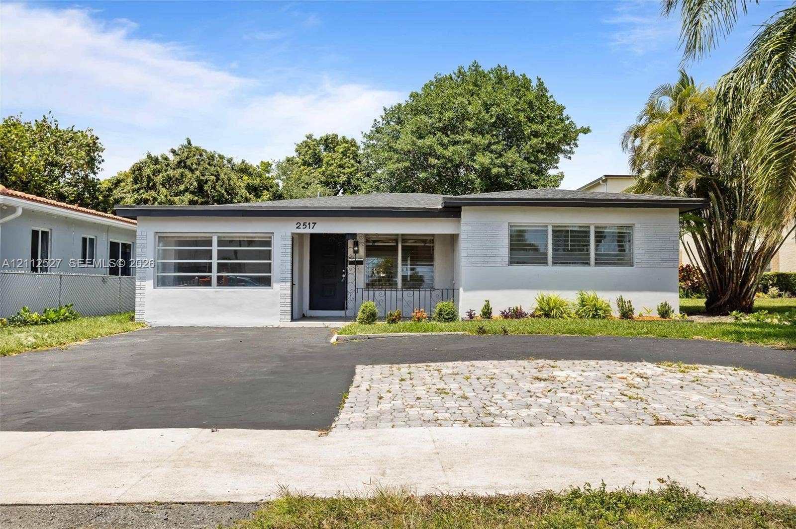 2517 Polk Street, Hollywood, Hollywood, FL 33020 Single-story exterior featuring a painted brick facade, low-slope roofline, mixed asphalt and paver driveway, and multi-pane horizontal windows