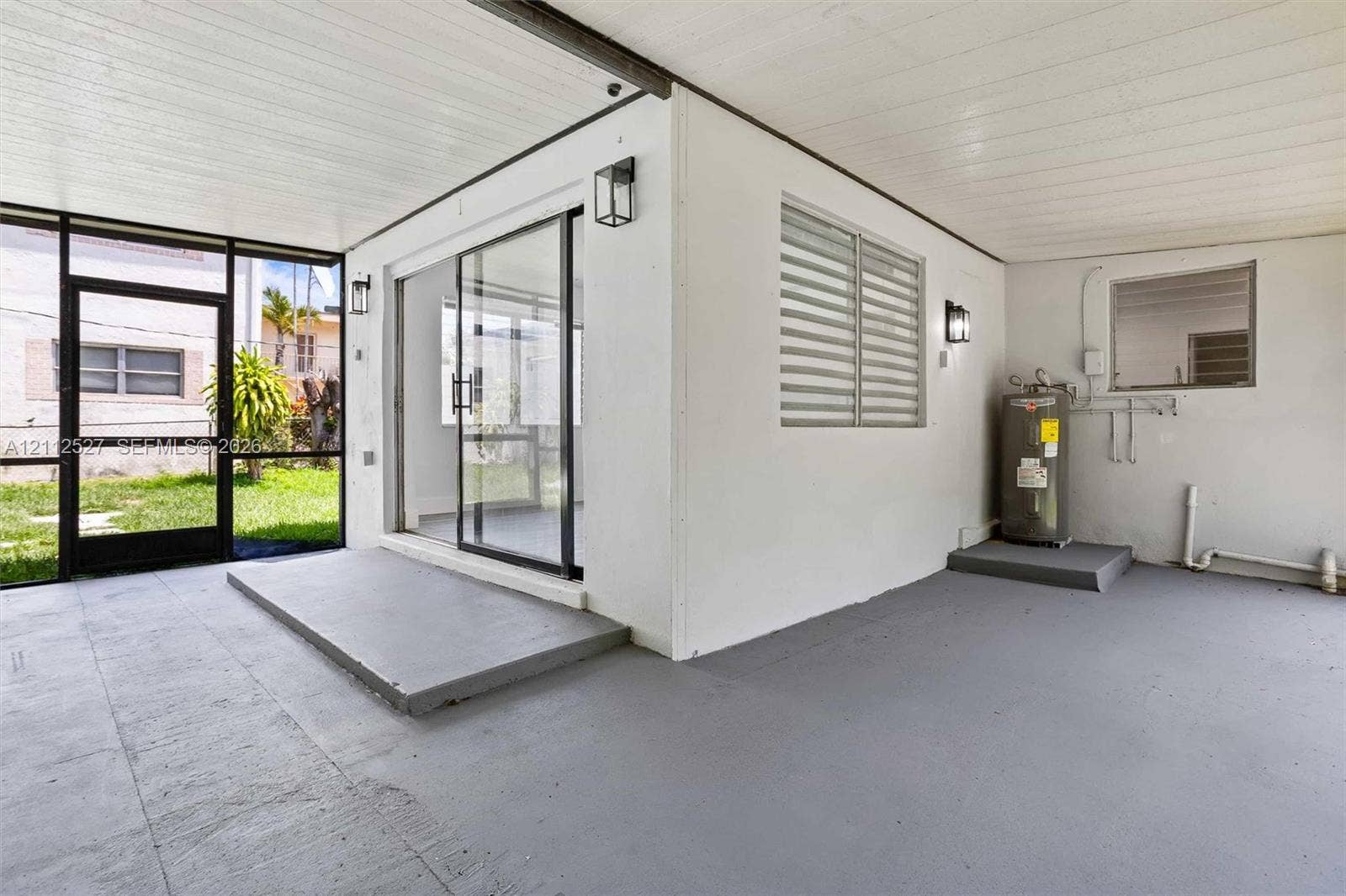 2517 Polk Street, Hollywood, Hollywood, FL 33020 Covered patio featuring a painted concrete floor, glass sliding doors, jalousie windows, exterior wall-mounted lighting fixtures, and a dedicated utility platform