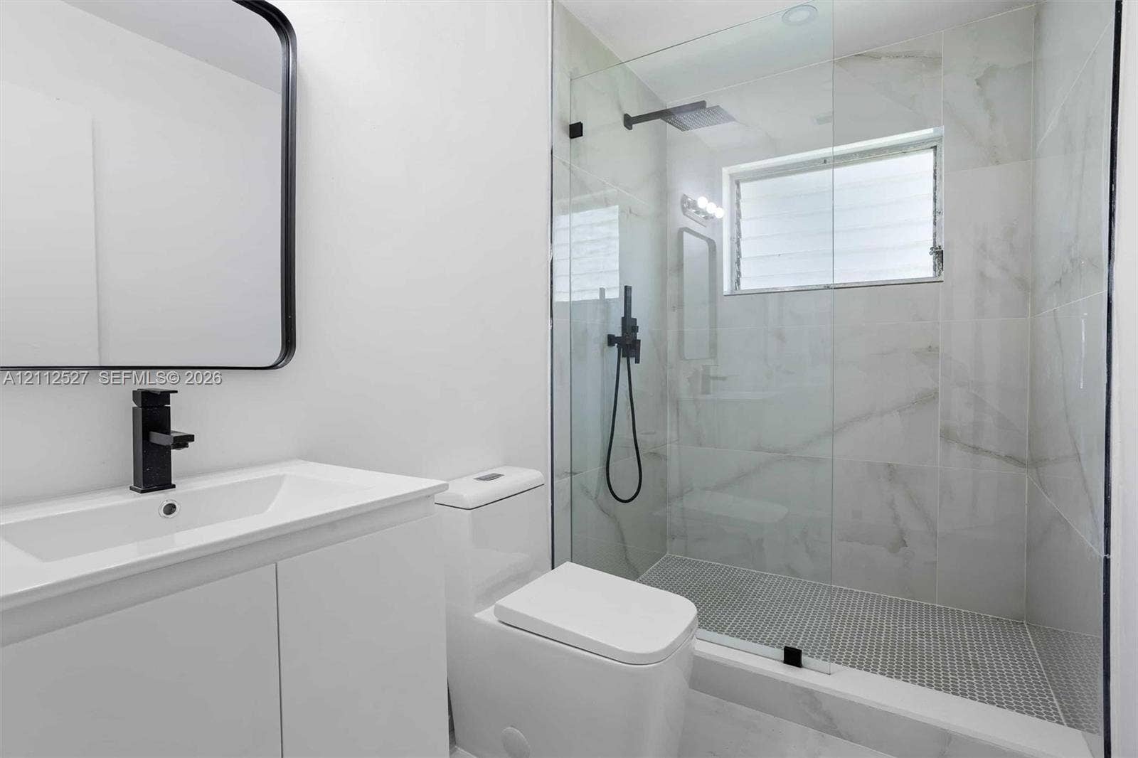 2517 Polk Street, Hollywood, Hollywood, FL 33020 White vanity with a rectangular sink, matte black faucet, wall-mounted mirror, walk-in shower with large-format tile surround, and black rainfall shower head