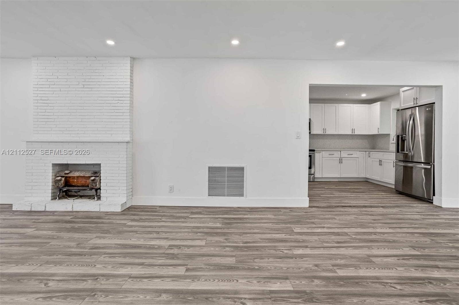2517 Polk Street, Hollywood, Hollywood, FL 33020 Interior space featuring wood-finish flooring, white brick fireplace with a wood-burning insert, recessed lighting, and kitchen area with white cabinetry and stainless steel appliances