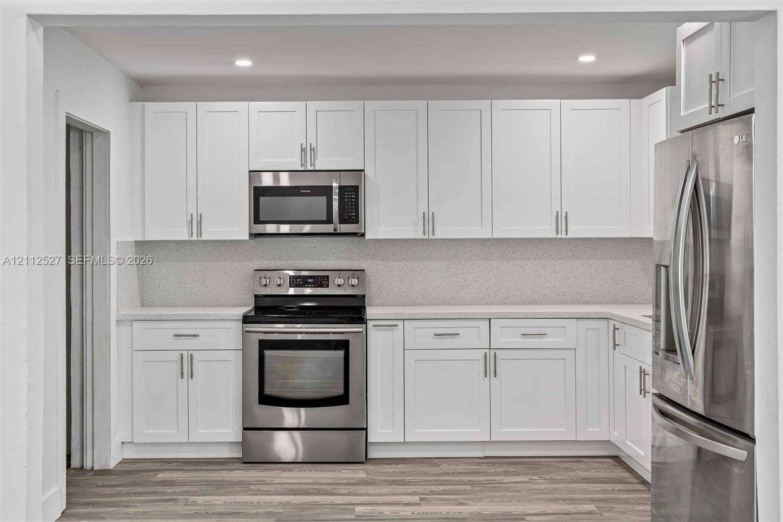 2517 Polk Street, Hollywood, Hollywood, FL 33020 Kitchen featuring white shaker-style cabinetry, stainless steel appliances, speckled stone-composite backsplash, light-toned solid surface countertops, and wood-finish flooring