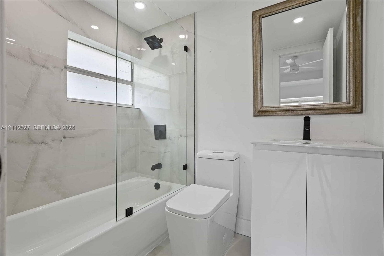 2517 Polk Street, Hollywood, Hollywood, FL 33020 Bathroom featuring a glass-enclosed shower and tub combination, large-format tile surround, modern white vanity with a single-basin sink, and matte black plumbing fixtures
