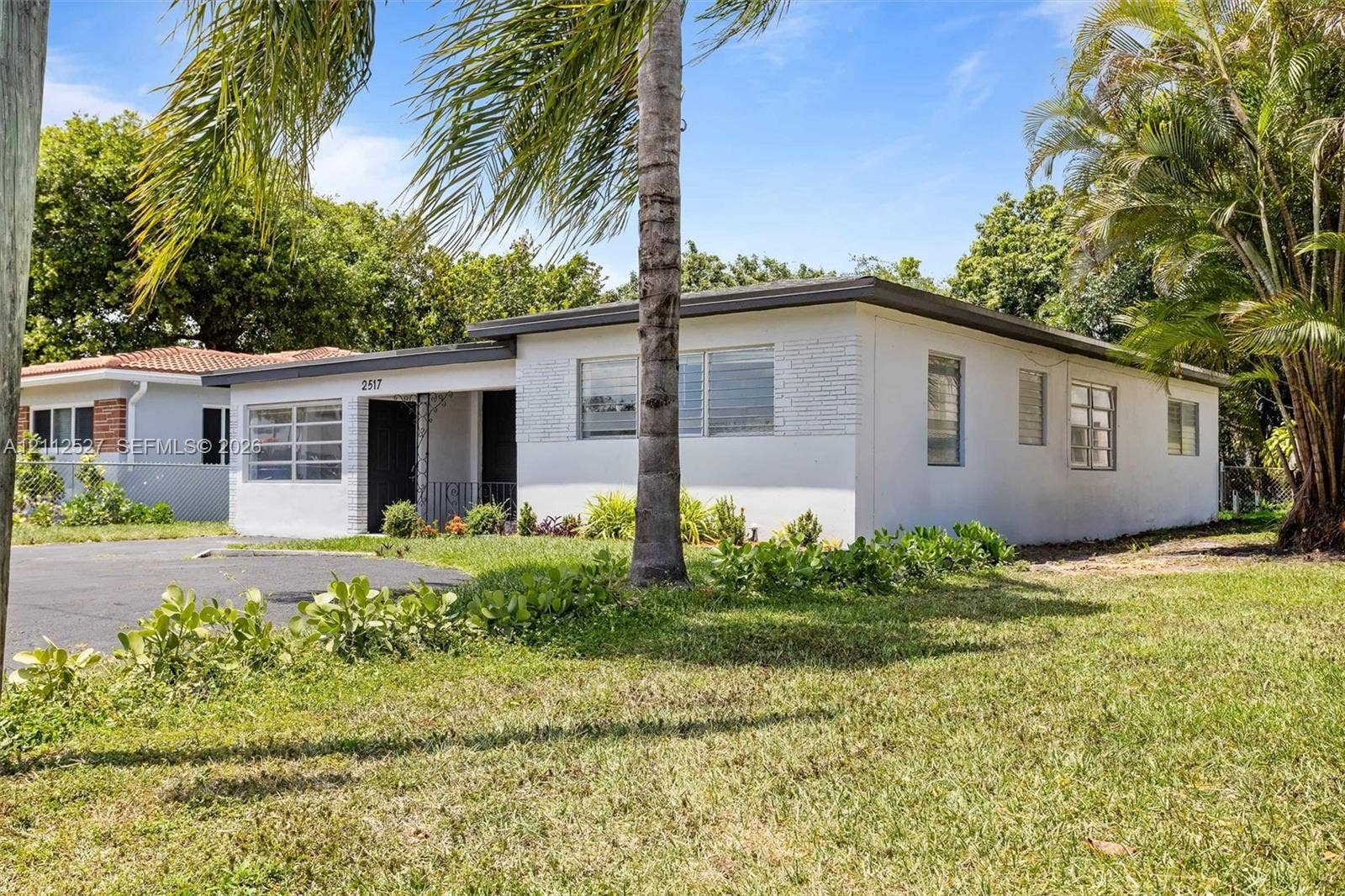 2517 Polk Street, Hollywood, Hollywood, FL 33020 Single-story exterior featuring a light-toned smooth finish, partial brick facade accents, horizontal louvered windows, and mature landscaping