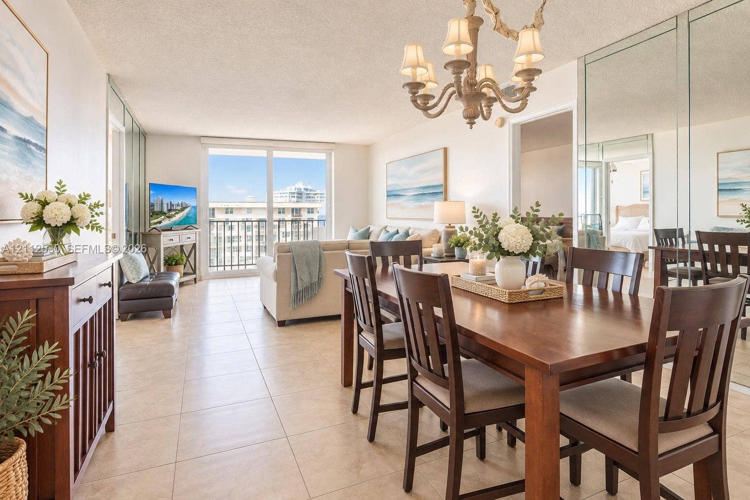 Open-concept living and dining area featuring large-format ceramic tile flooring, a multi-arm chandelier, full-height wall mirrors, and floor-to-ceiling sliding glass doors leading to a balcony