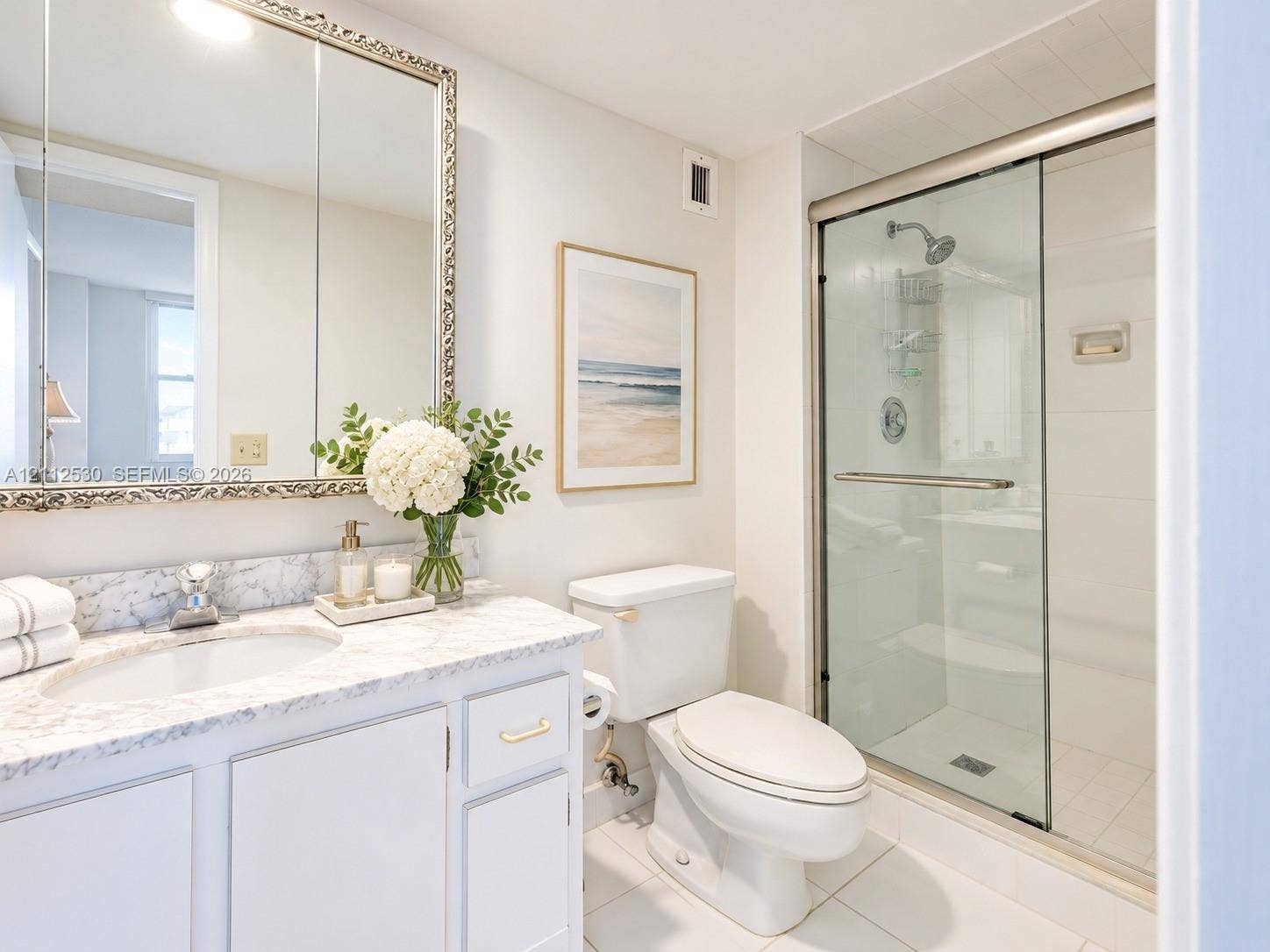 Bathroom featuring white cabinetry, stone-surface countertop, integrated vanity sink, large wall-mounted mirror, and a glass-enclosed shower with metallic hardware