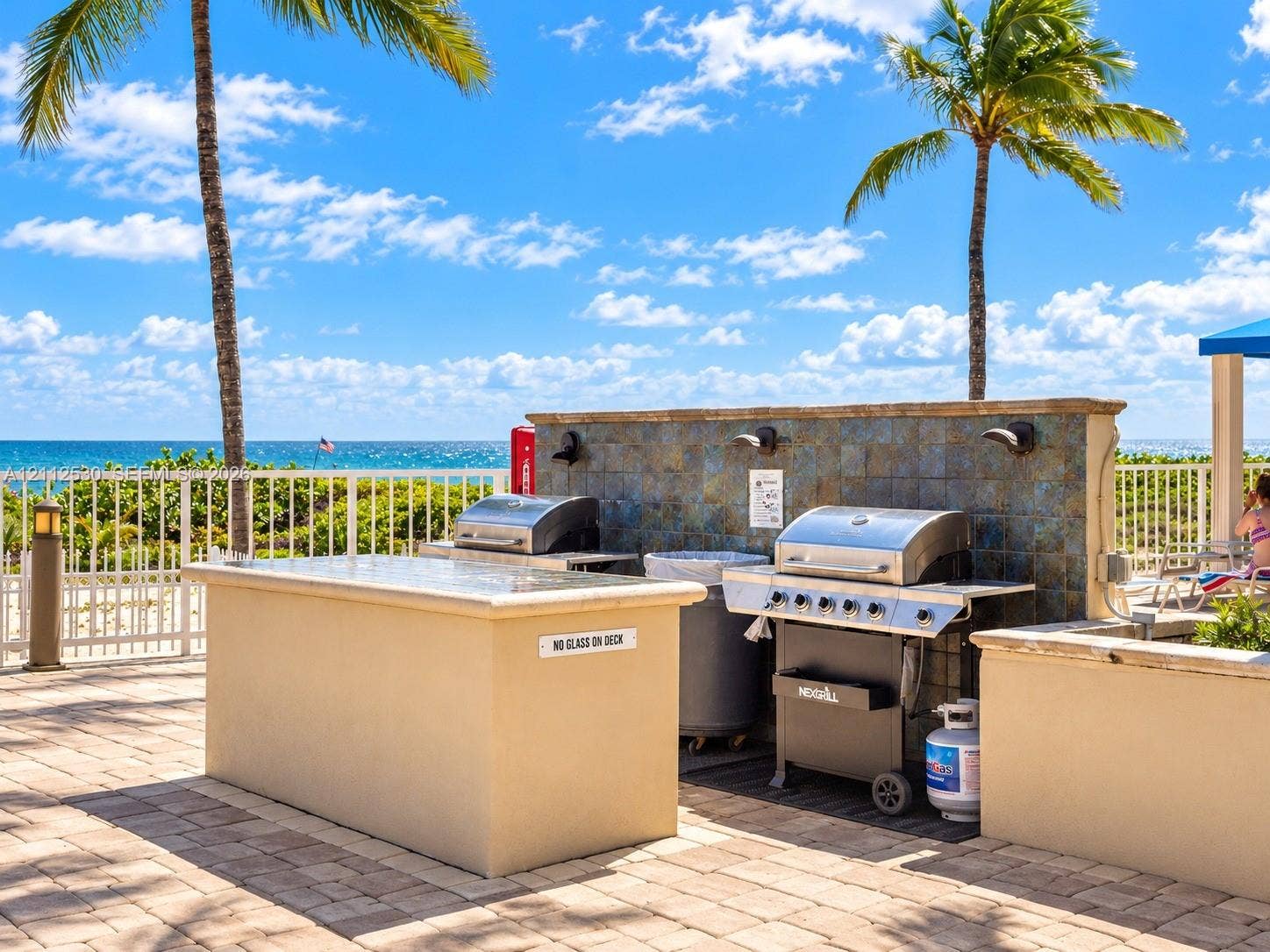 Outdoor kitchen area featuring a stone-tile backsplash, concrete countertops, stainless steel grill, and paver patio flooring