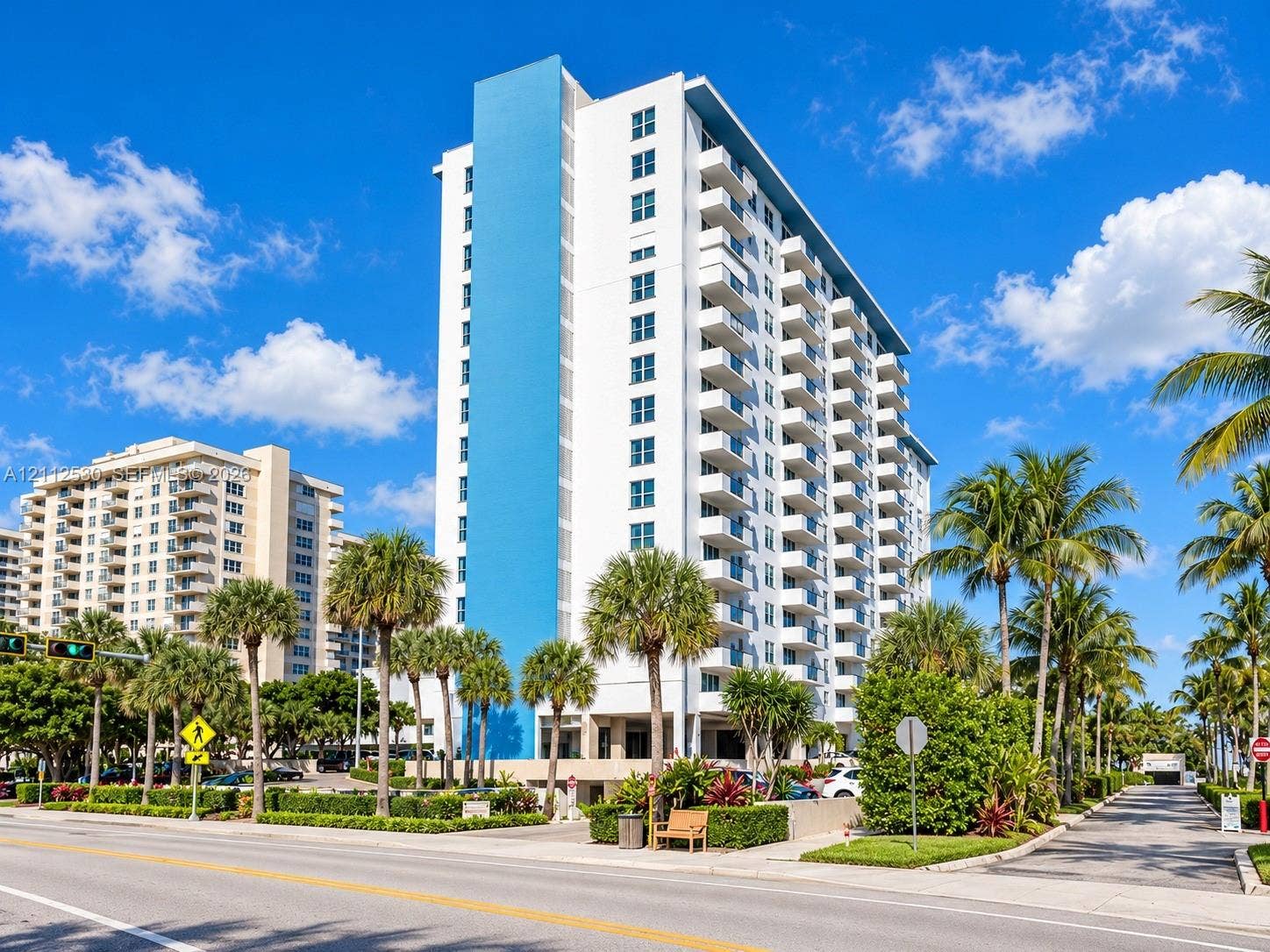 High-rise building featuring a white and blue exterior, stacked balconies, and manicured tropical landscaping