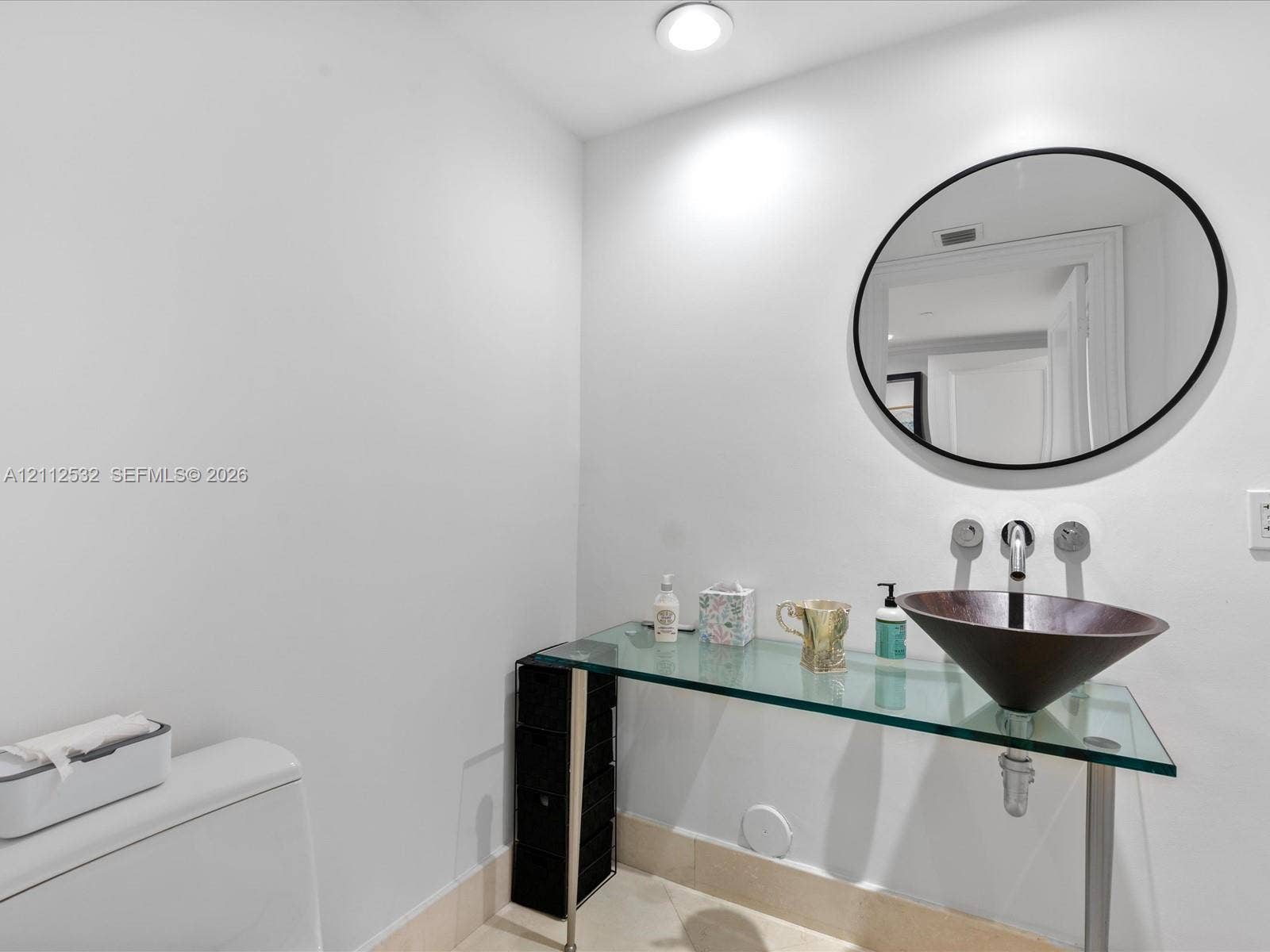 18911 Collins Avenue, #601, Sunny Isles Beach, FL 33160 Glass-topped vanity featuring a conical vessel sink, wall-mounted faucet, and minimalist circular mirror