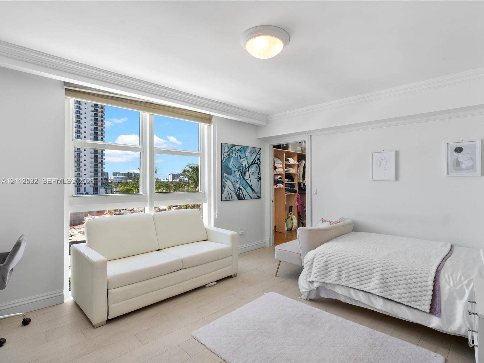 18911 Collins Avenue, #601, Sunny Isles Beach, FL 33160 Light-filled room featuring wide-plank wood-finish flooring, extensive multi-pane windows, crown molding, and built-in closet cabinetry