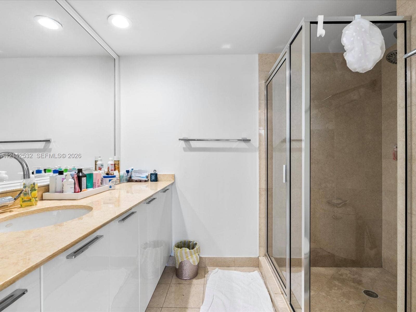 18911 Collins Avenue, #601, Sunny Isles Beach, FL 33160 Bathroom featuring a wide vanity with high-gloss white cabinetry, a stone-surfaced countertop, a wall-to-wall mirror, and a walk-in shower enclosure with tile walls