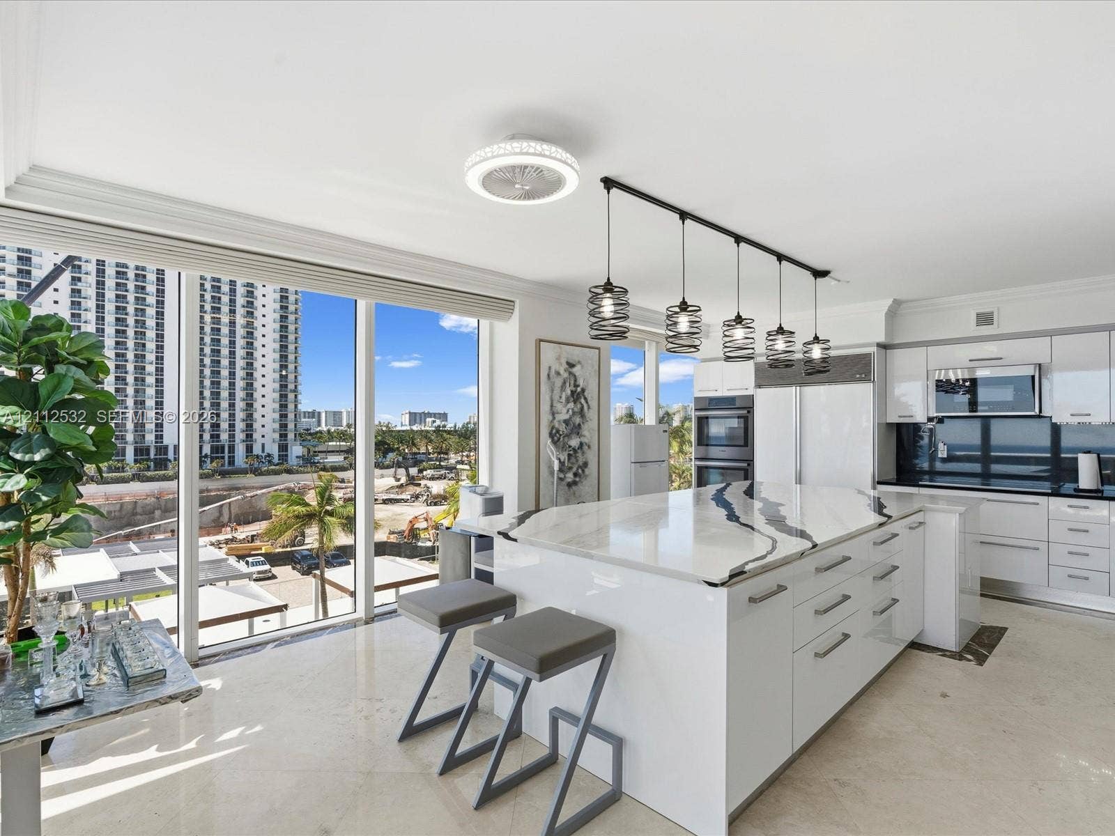 18911 Collins Avenue, #601, Sunny Isles Beach, FL 33160 Kitchen featuring high-gloss cabinetry, stone-topped center island with waterfall edge, built-in double wall ovens, five-light linear pendant fixture, and floor-to-ceiling windows